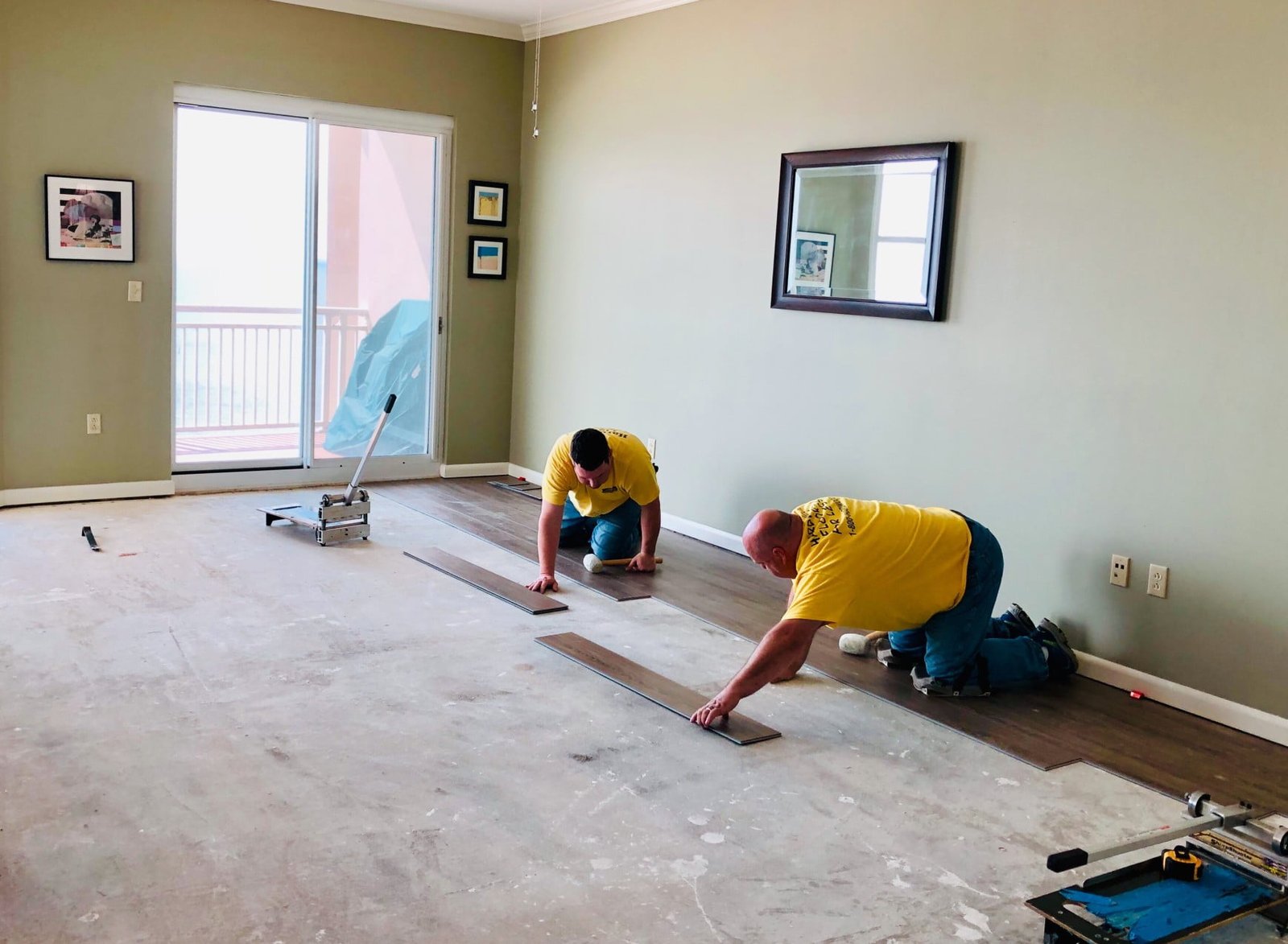Two men working on a hardwood floor in a living room.
