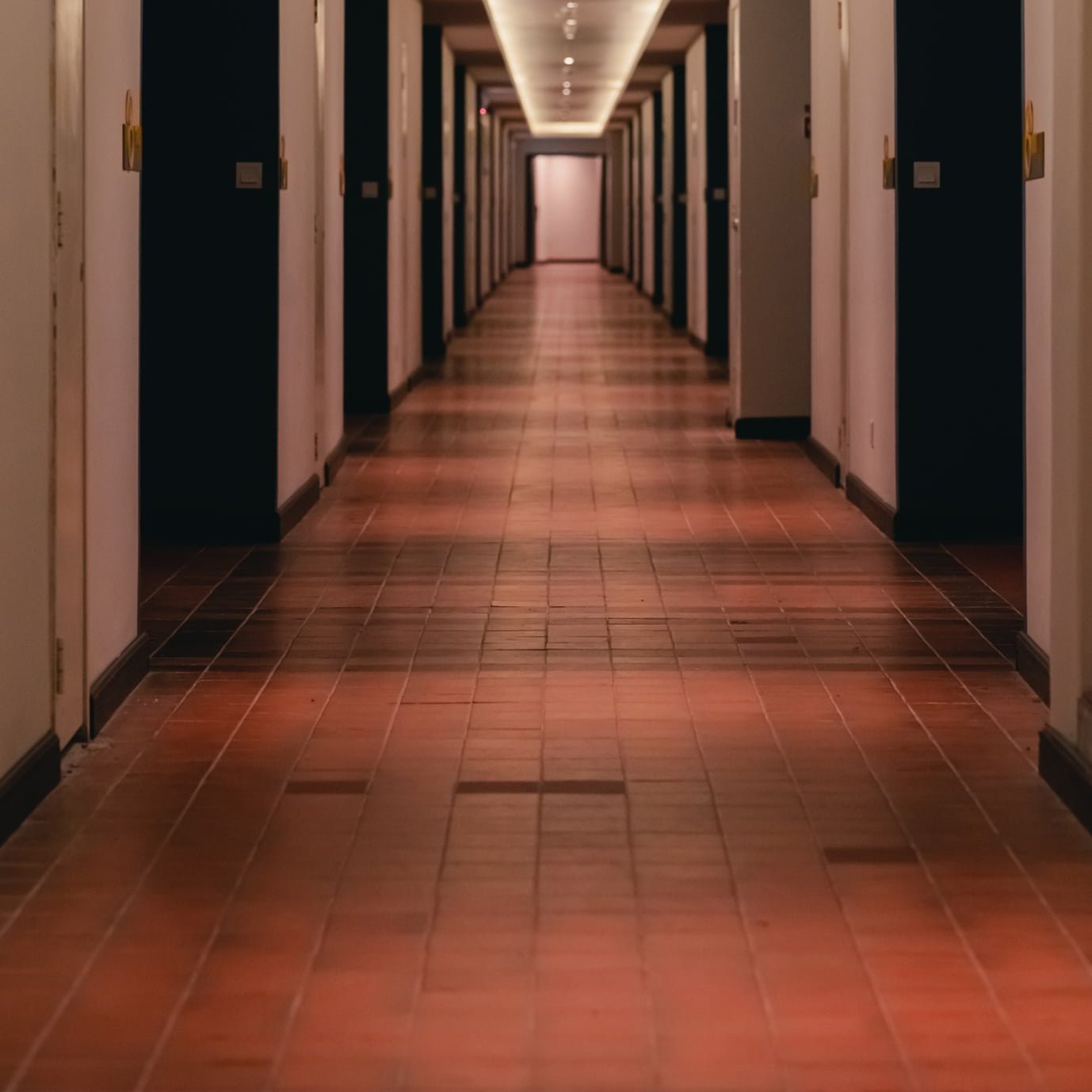A hallway in a hotel with red tiled floors.